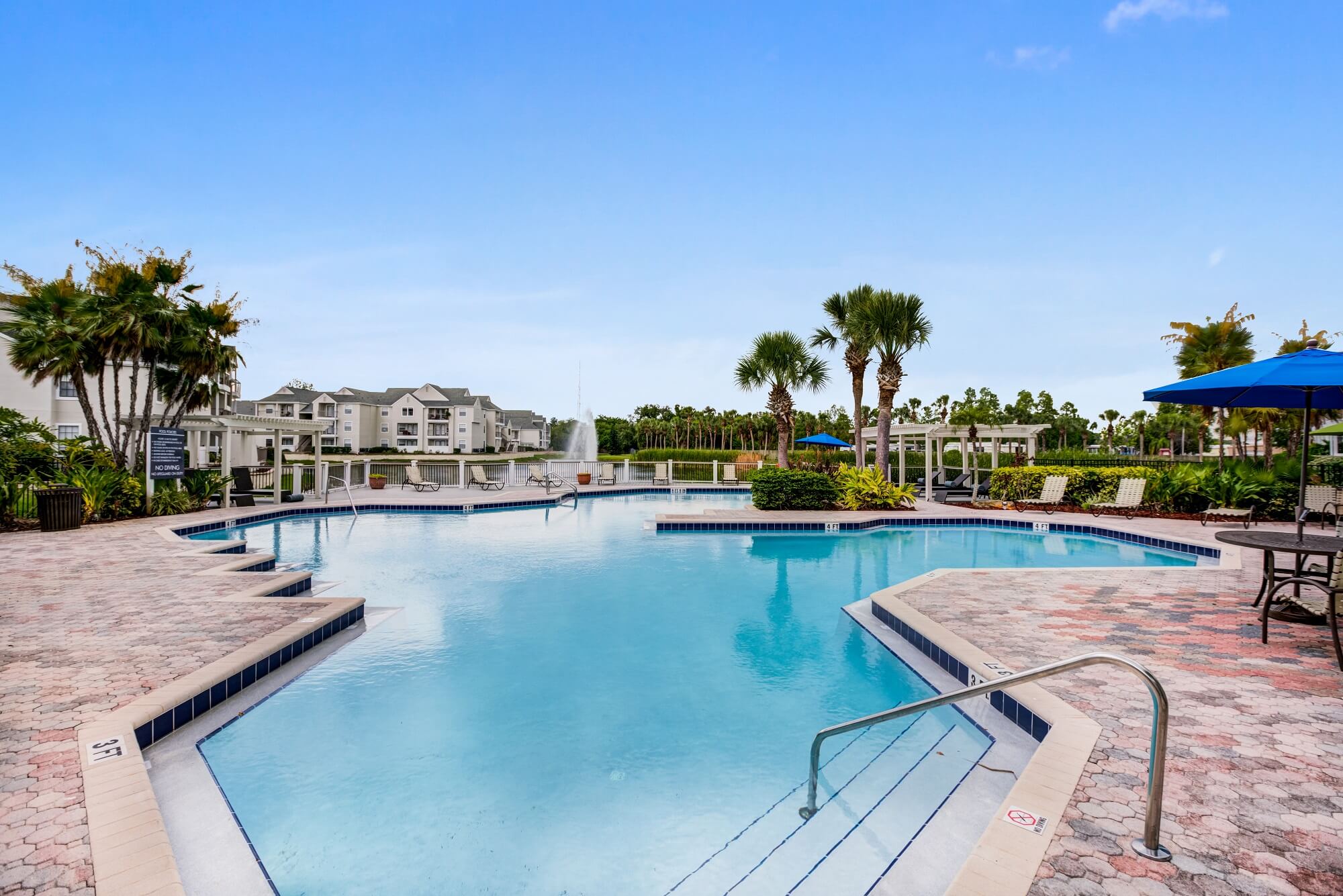 large pool with lounge chairs, seating, umbrellas, and palm trees.
