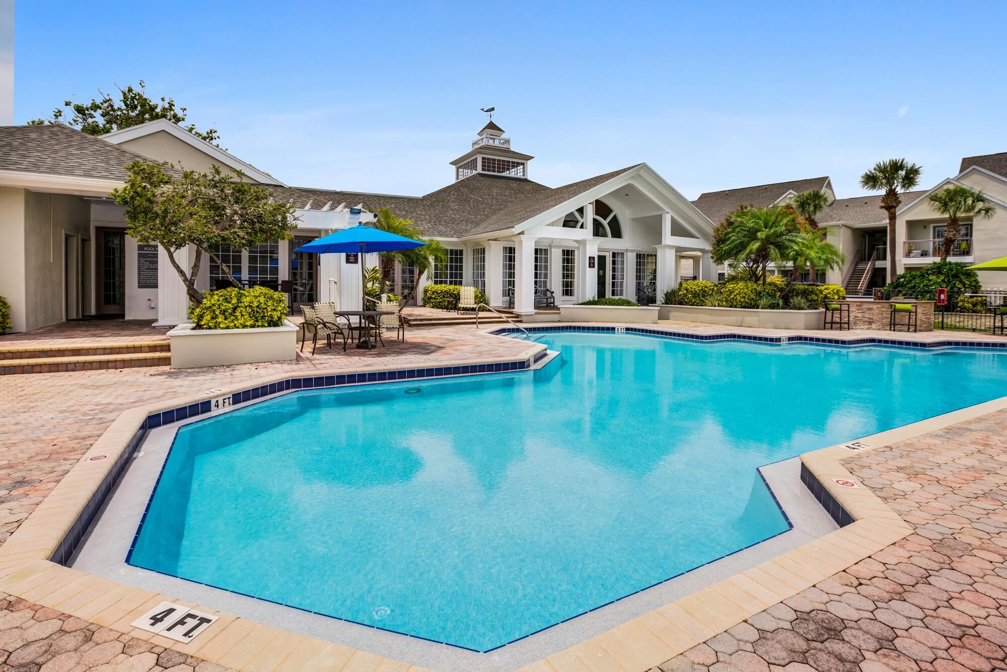 large pool with chairs, seating, umbrellas, and view of clubhouse.