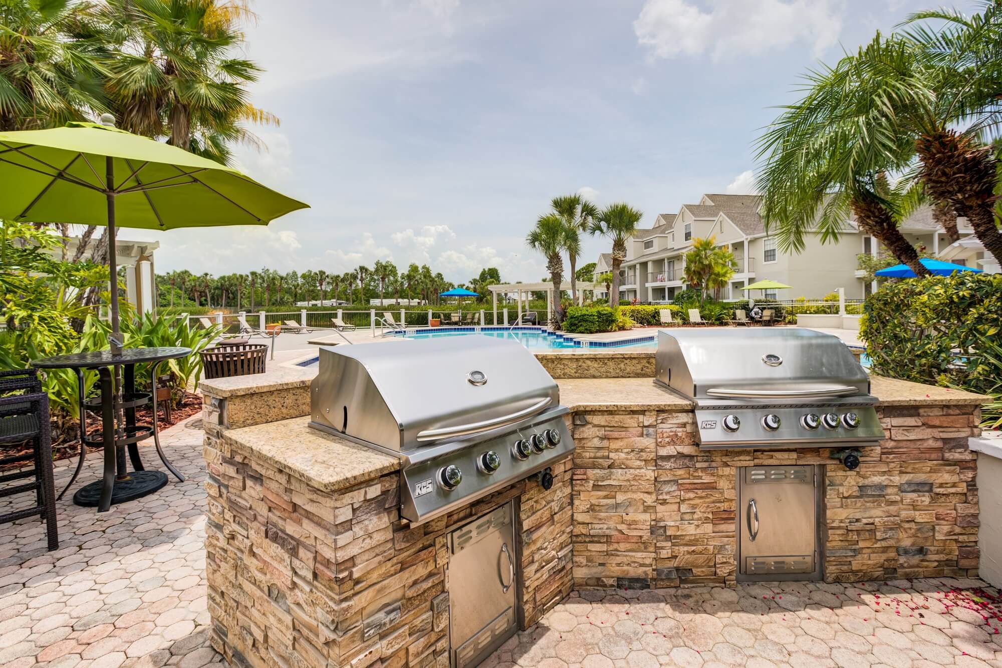 two 4 burner grills with stone countertops with view of the pool.