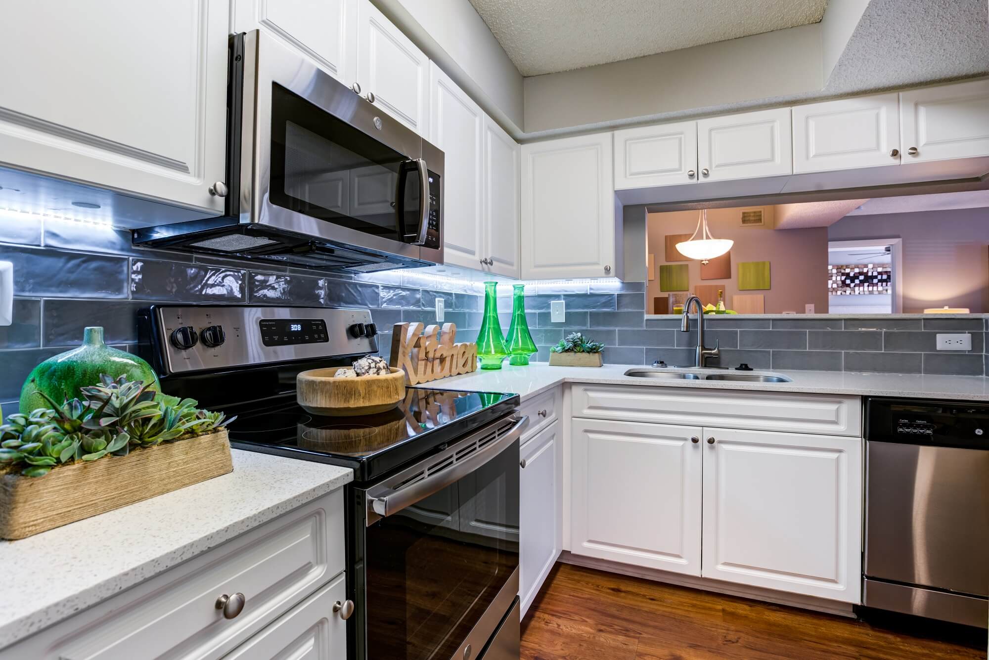 l-shaped kitchen with white cabinets, tiled backsplash, stove, microwave, and dishwasher.